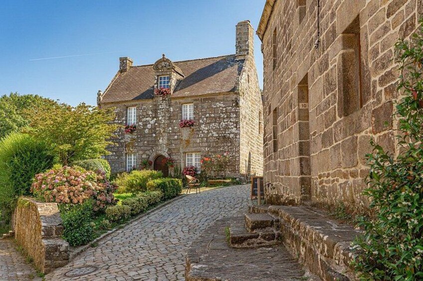 A stone building with a cobblestone path leading to it, surrounded by greenery and flowers. 4