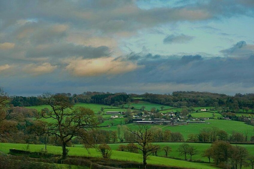 A rural landscape with rolling green fields, a small village, and a cloudy sky. 2
