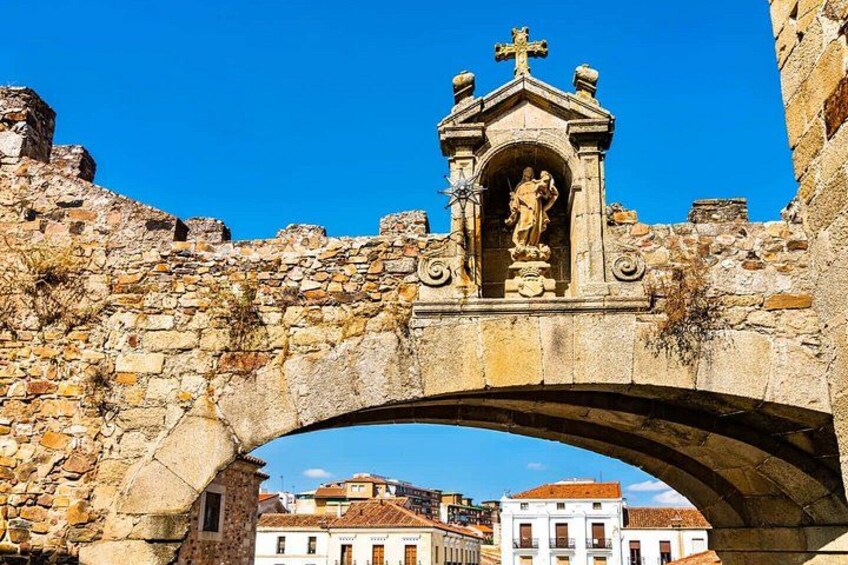 A stone bridge with a statue on top, surrounded by buildings. 2