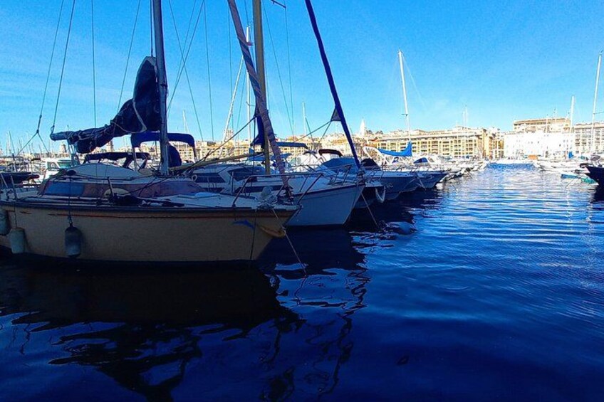 A marina with several sailboats docked, calm water, and buildings in the background. 2