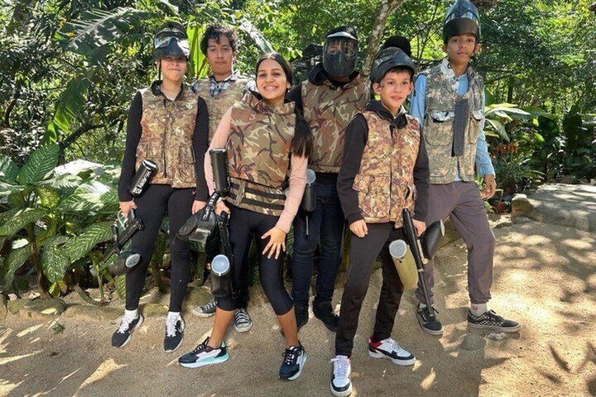 A group of people in camouflage attire with paintball gear, standing in a natural setting with trees and foliage. 5