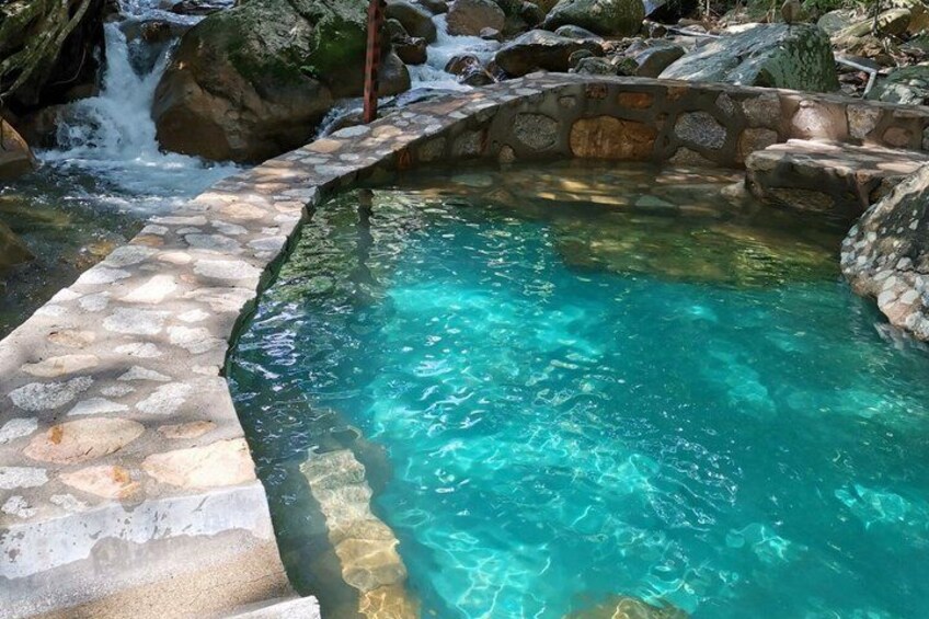 A stone pool with clear water, surrounded by rocks and a small waterfall. 3