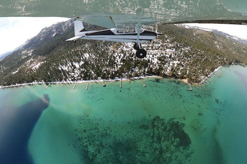 An airplane flying over a coastal area with a forested mountain in the background and a clear turquoise sea. 5
