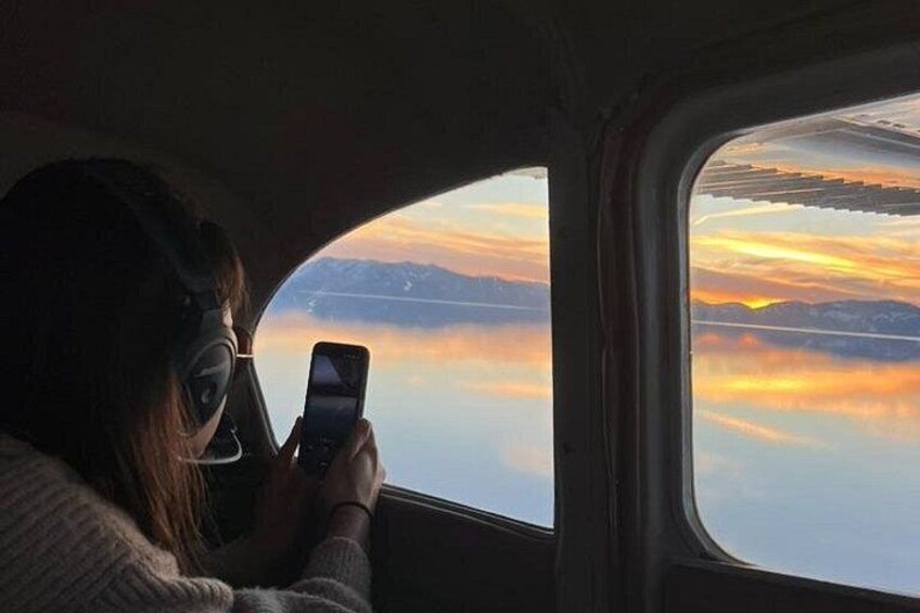 A person using a smartphone inside a vehicle, with a view of a sunset over water and mountains. 3