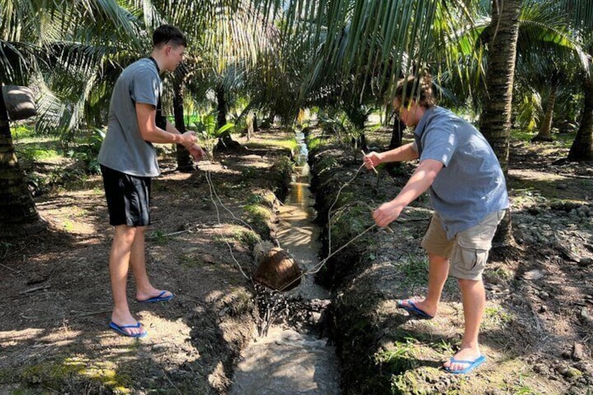 Twee mensen vissen in een tropische omgeving met palmbomen en een beekje. 4