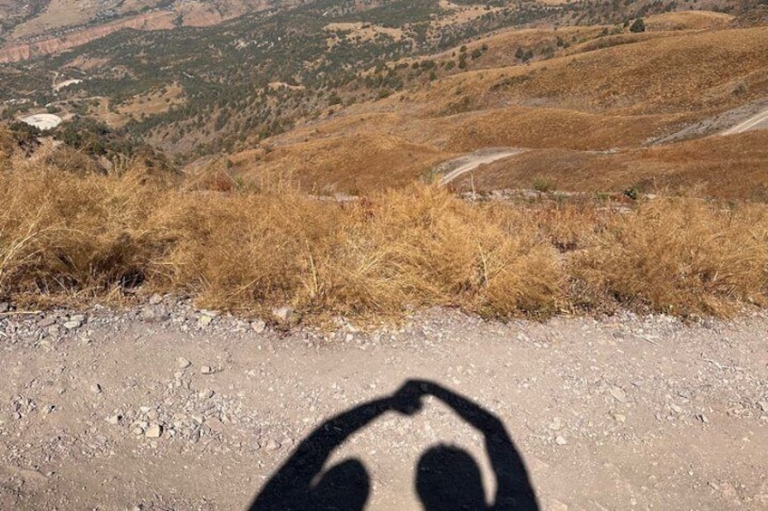 A shadow of a person on a dirt road with dry grass and a hilly landscape in the background. 4