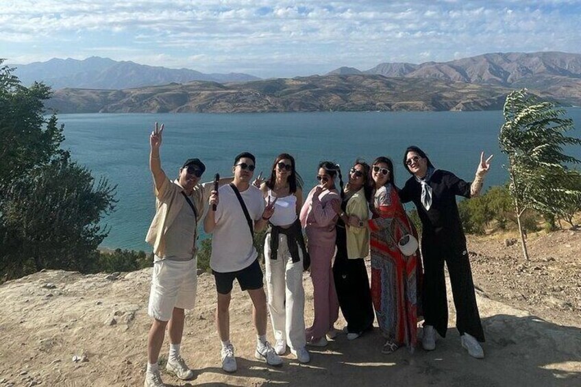 A group of people posing on a rocky outcrop with a lake and mountains in the background. 1