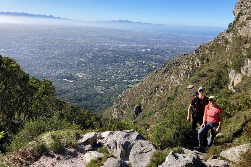 Dos excursionistas en un sendero rocoso de montaña con un paisaje urbano al fondo. 5