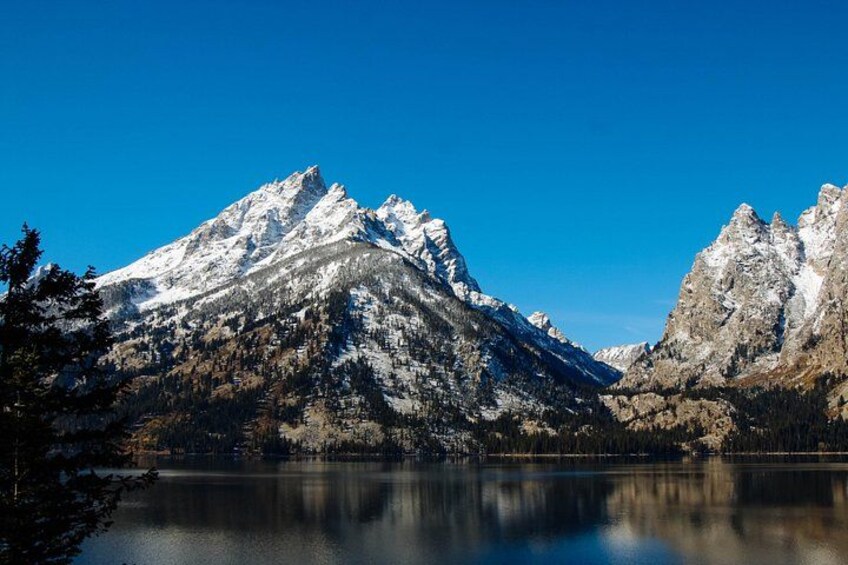 A mountain range with snow-capped peaks, a calm lake, and a clear blue sky. 2
