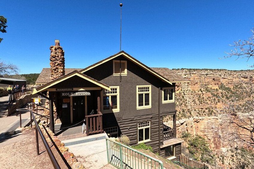 A wooden building with a stone chimney, labeled 'KOLB STUDIO,' set against a rocky canyon backdrop. 5