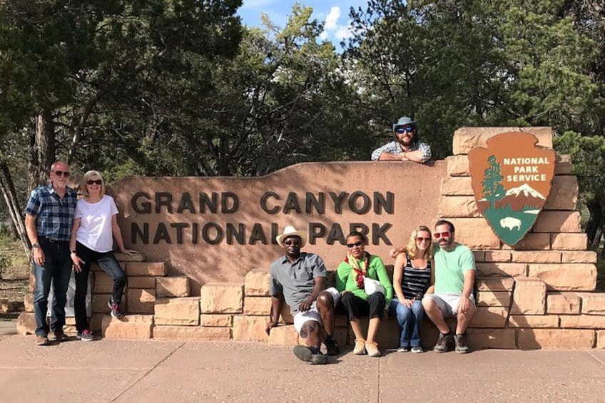 A group of people posing in front of the Grand Canyon National Park sign. 4