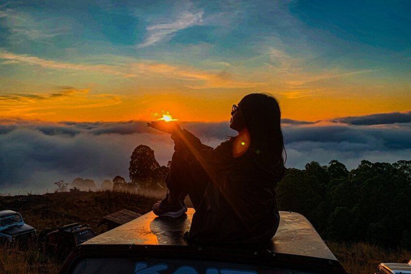 A person sitting on a vehicle, overlooking a landscape with a sunset and clouds. 4