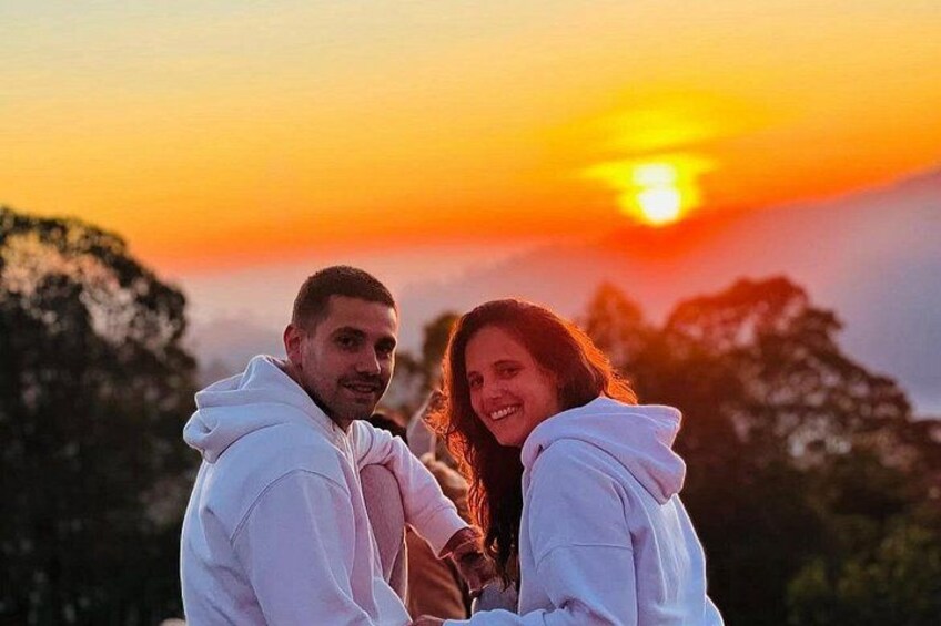 A sunset with a couple embracing, wearing white hoodies, with trees in the background. 3