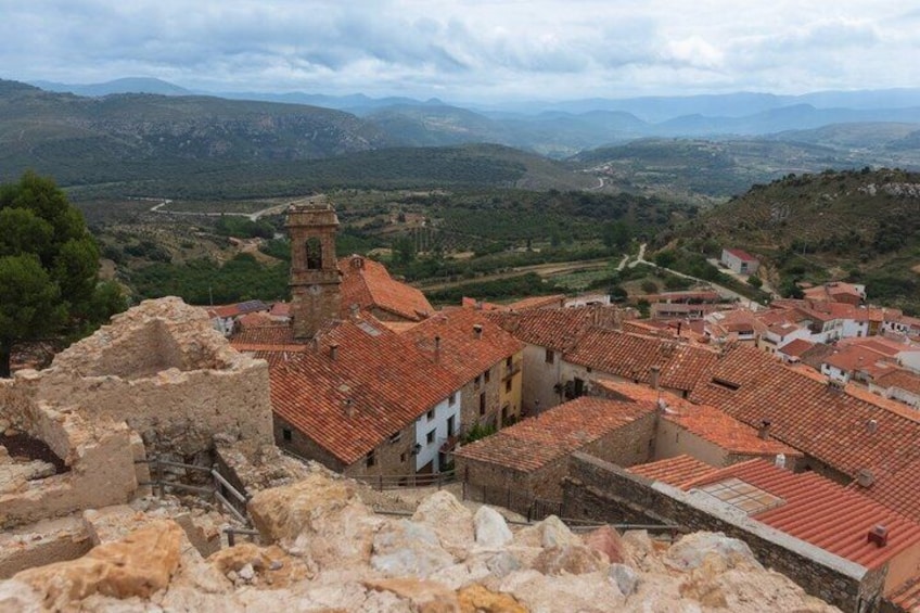 A historic town with red-tiled roofs, a prominent church tower, and surrounding hills. 2