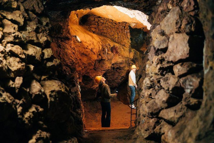 A cave with a person standing on a ledge and another person inside. 1