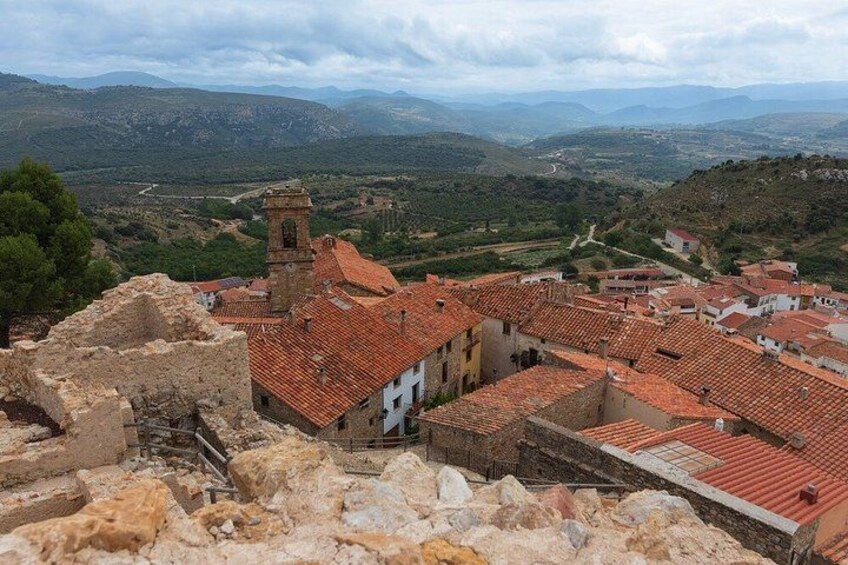 A historic town with terracotta-roofed buildings, a prominent church tower, and a mountainous backdrop. 2