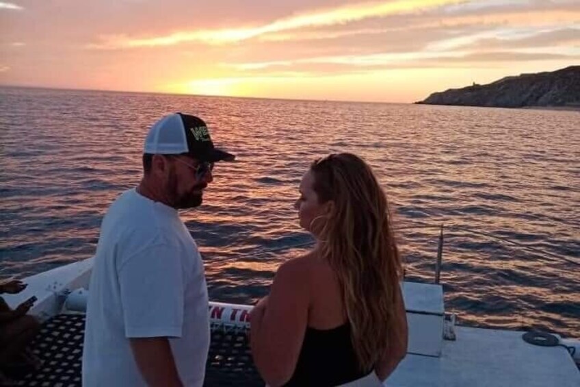 A couple on a boat during sunset with the ocean and a distant landmass in the background. 2