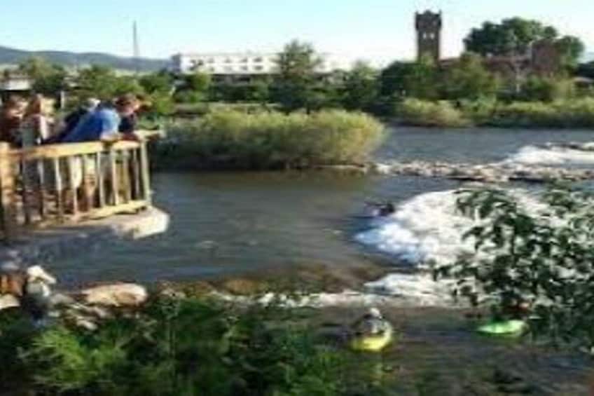 Un río con un puente de madera, personas en el puente y kayaks en el agua. 2