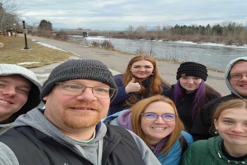 A group of people outdoors near a river with a bridge in the background. 2