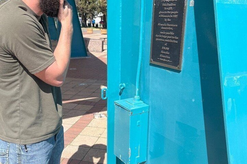 Una persona tomando una foto a una estructura azul y una placa con texto. 3