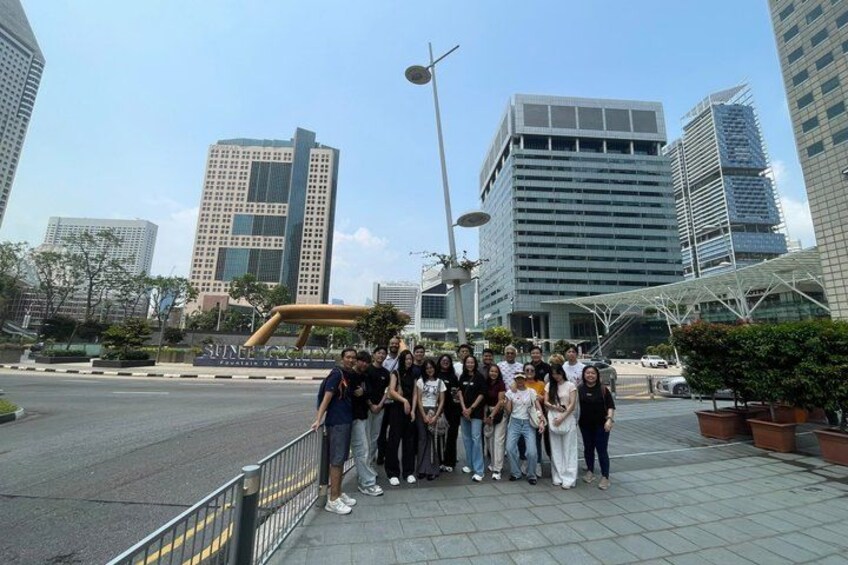 Eine Gruppe von Menschen posiert in einem städtischen Umfeld mit modernen Gebäuden und einer Straßenlaterne im Hintergrund. 2