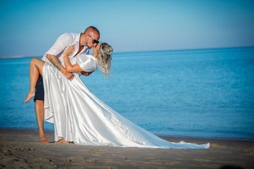 Ein Paar am Strand, wobei ein Mann eine Frau in einem weißen Kleid hochhebt. 1