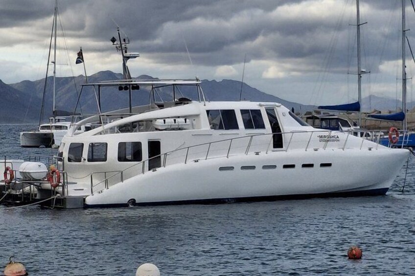 En vit lyxyacht låg förtöjd vid en småbåtshamn med berg i bakgrunden. 2
