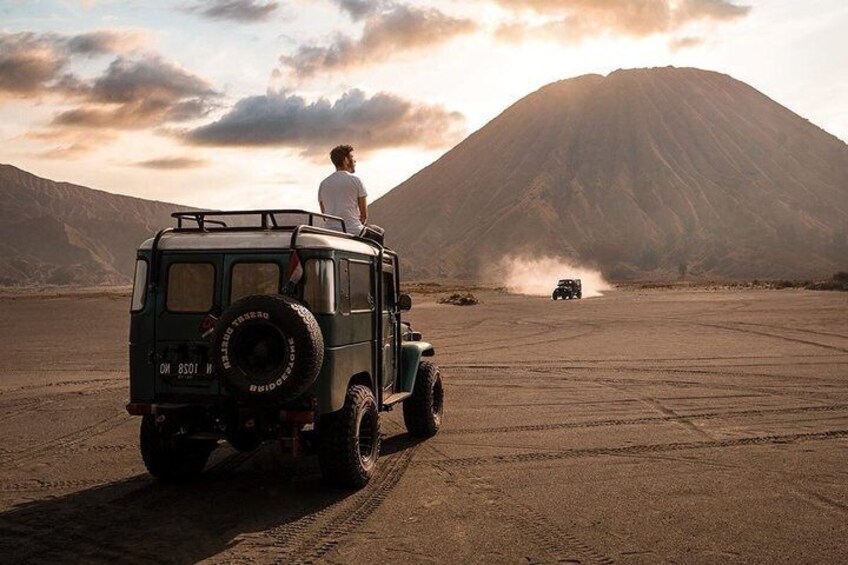 A person driving a green off-road vehicle on a dirt road with a mountain in the background. 5
