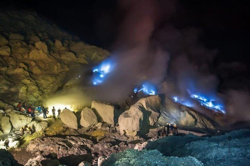 A group of people at a geothermal site with visible steam and glowing rocks. 3