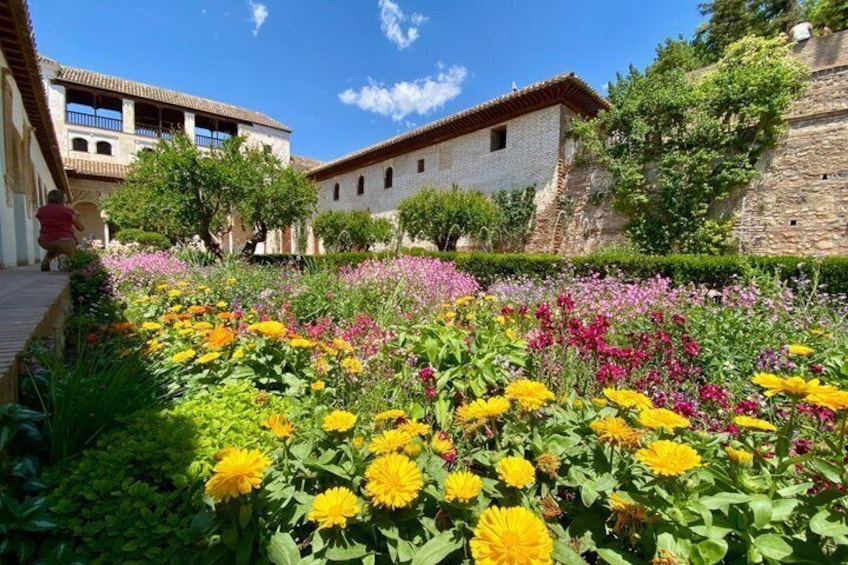 A courtyard with colorful flowers, stone buildings, and a clear blue sky. 5