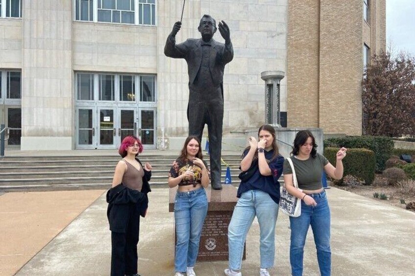 Four people posing in front of a statue and a building. 1