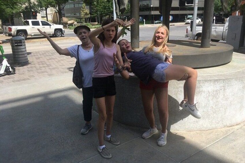 Four people posing in a public square with a circular structure and a white pickup truck in the background. 2