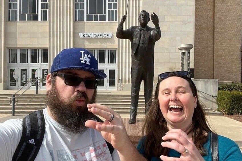 Two people in front of a building with a statue and a sign that reads 'BOX OFFICE'. 3