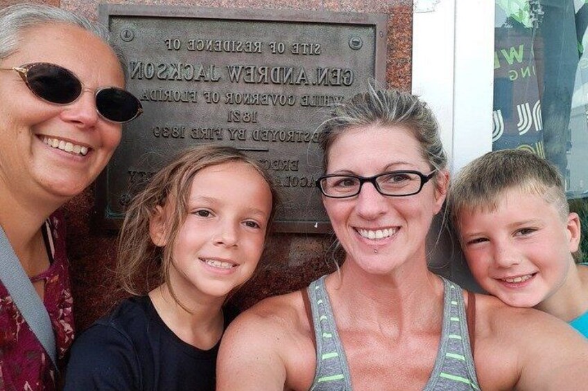 Una familia de cuatro personas frente a una placa conmemorativa histórica. 2