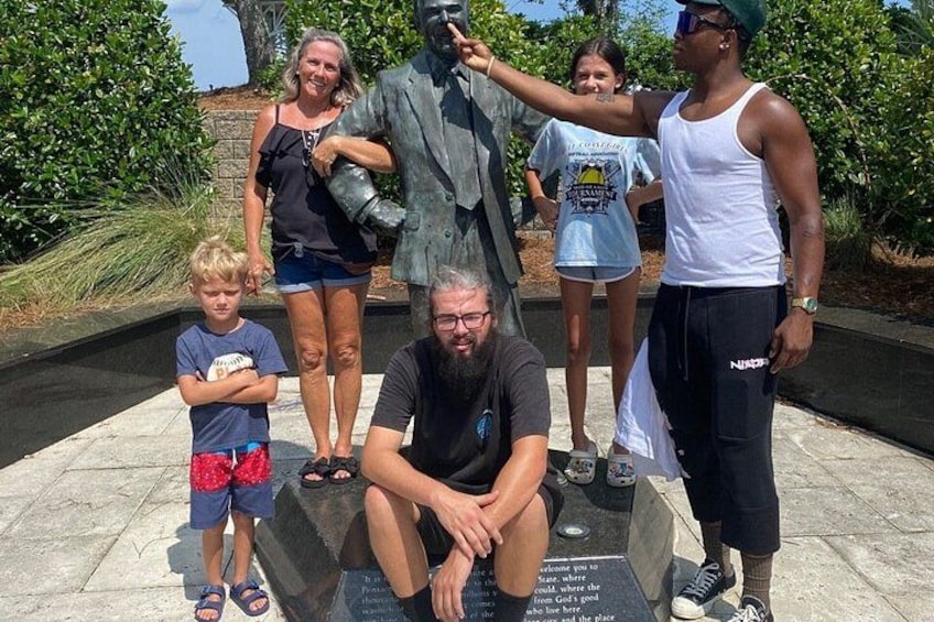 Una familia posa junto a una estatua de un hombre con traje y corbata. 3