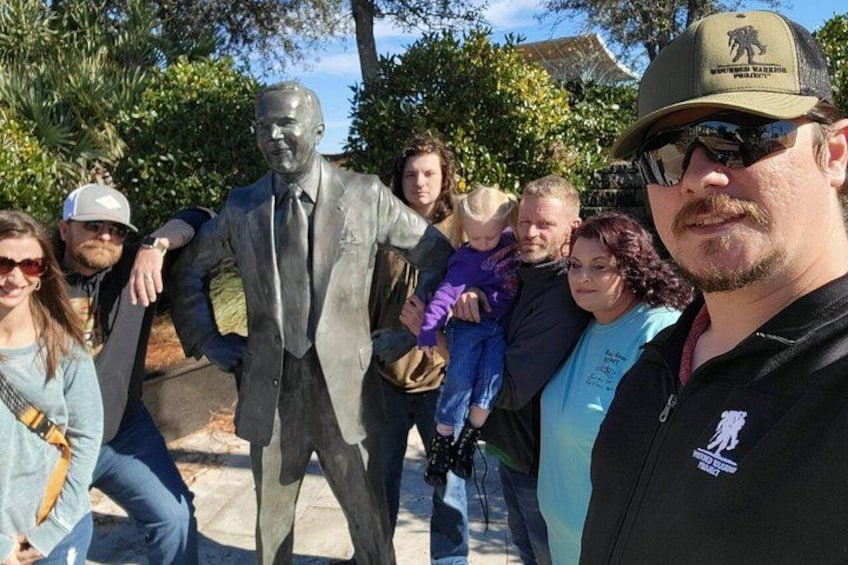 Un grupo de personas posando junto a una estatua de un hombre trajeado. 5