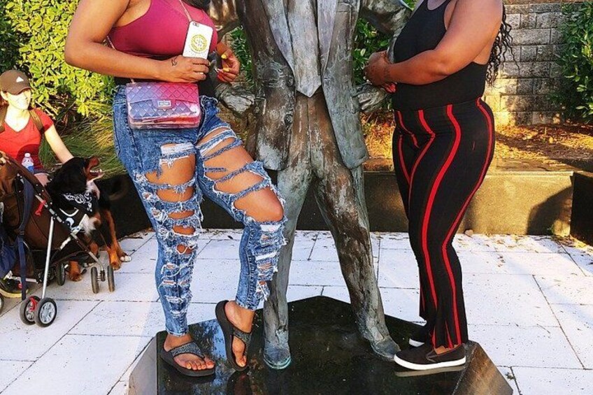 Una persona de pie junto a un árbol, sosteniendo un libro, con jeans rotos y una camiseta de tirantes. 5