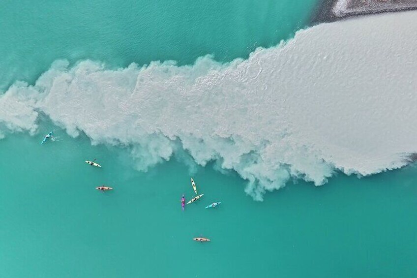 A turquoise sea with a large wave and several surfers. 5