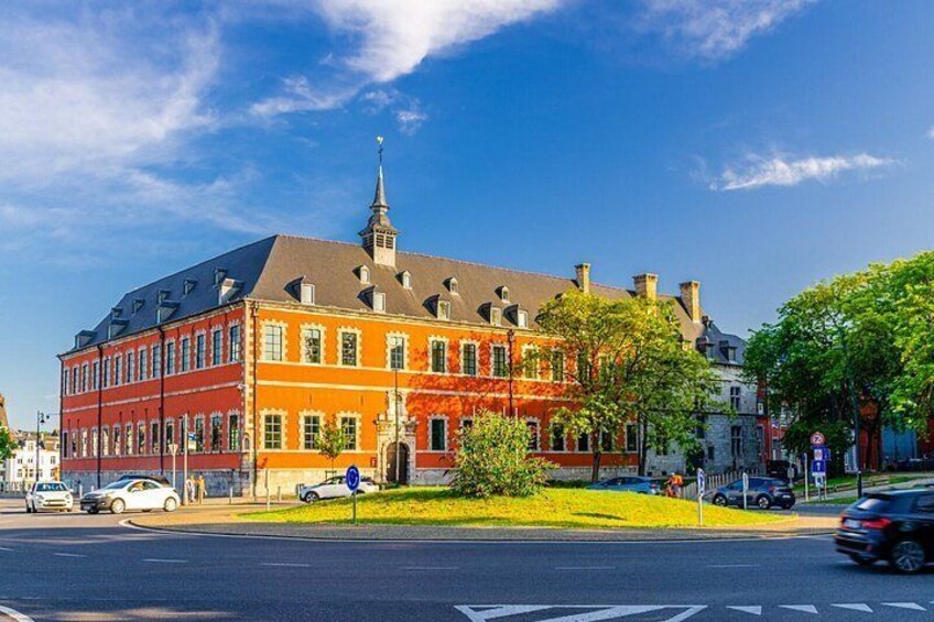 A red brick building with a tower, a street with cars, and a clear blue sky. 4
