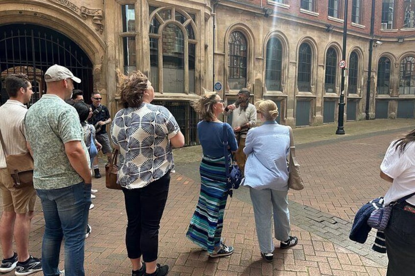 A group of people standing on a brick-paved street in front of a historic building with arched windows and a large archway. 2