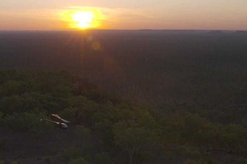 A sunset over a forested landscape with a vehicle on a road. 3