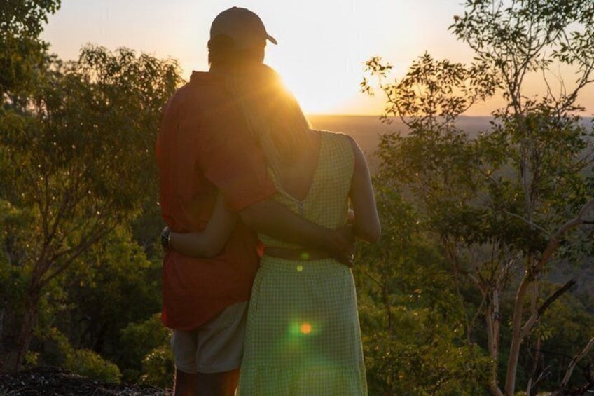 A couple embracing in a natural setting with trees and a sunset in the background. 2