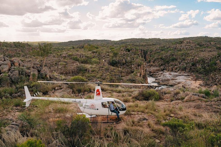 A helicopter with registration VH-LJD on a rocky terrain with sparse vegetation. 4
