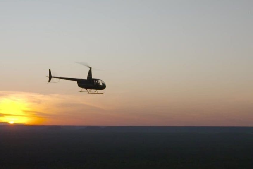 A helicopter flying over a landscape during sunset. 1
