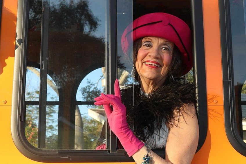 A person in a red hat and pink gloves leaning out of a bus window. 1