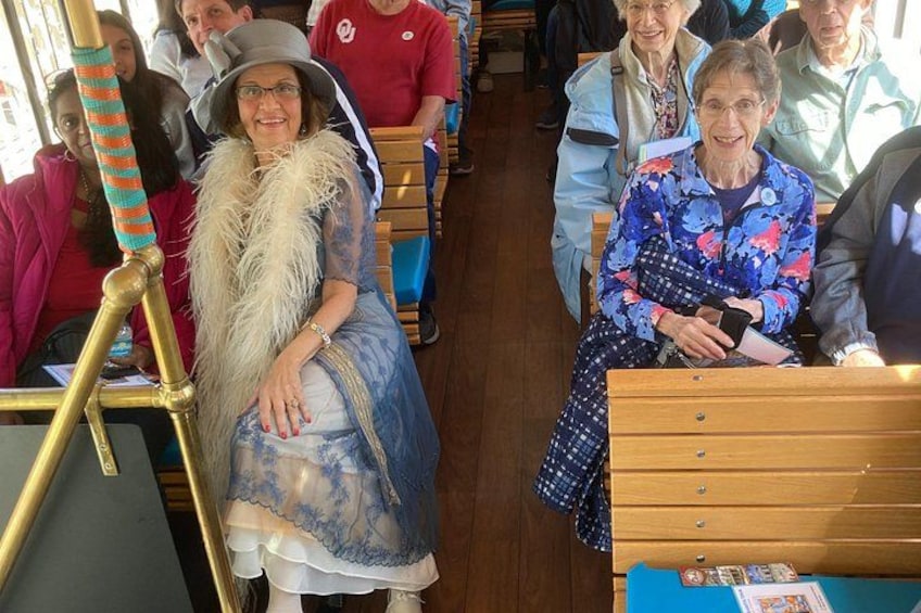 A person in a blue dress with a feather boa, seated on a bus. 4