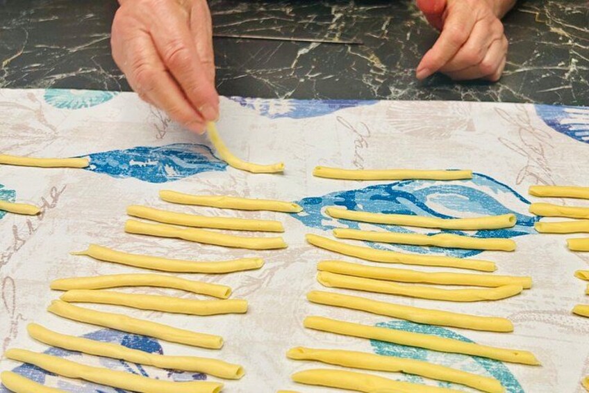 Hands shaping pasta dough into long, thin strips on a marble surface. 5