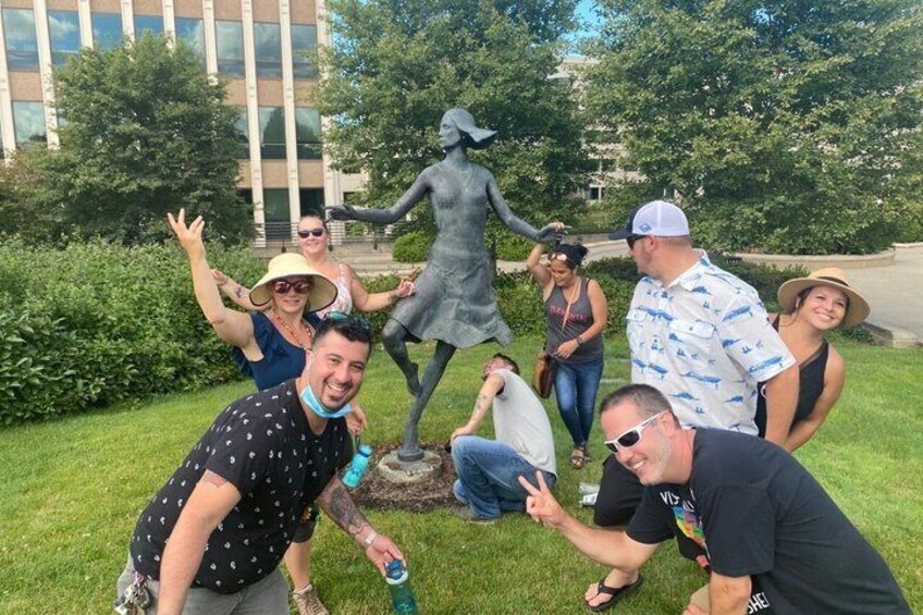 A group of people posing with a statue in a grassy area with trees and a building in the background. 4