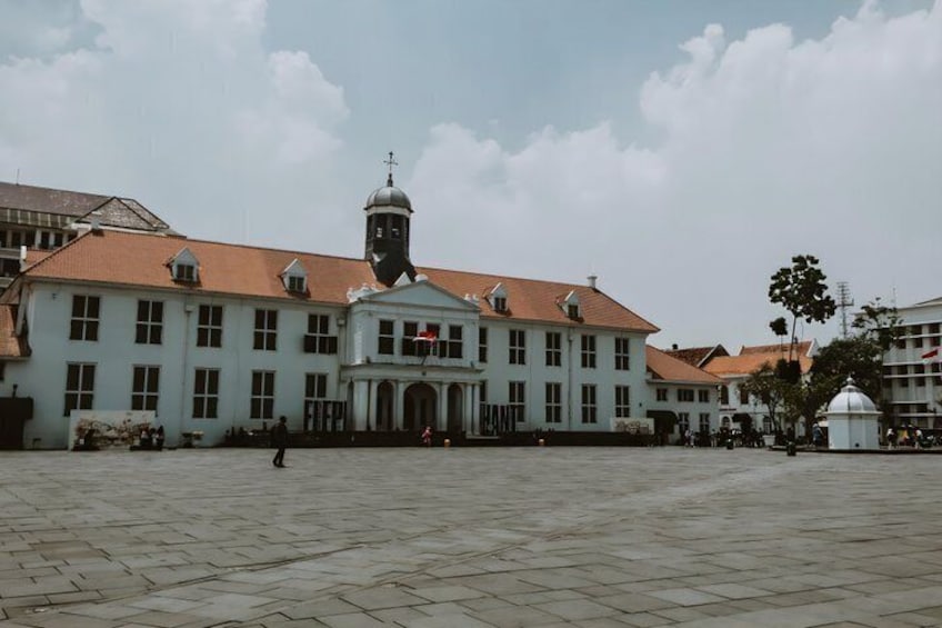 A large building with a clock tower, a central dome, and a paved courtyard. 5