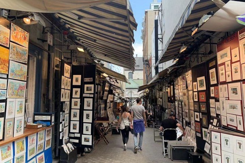 Eine enge Straße mit Kunstgalerien an beiden Seiten, Fußgänger und verschiedene Kunstwerke. 2